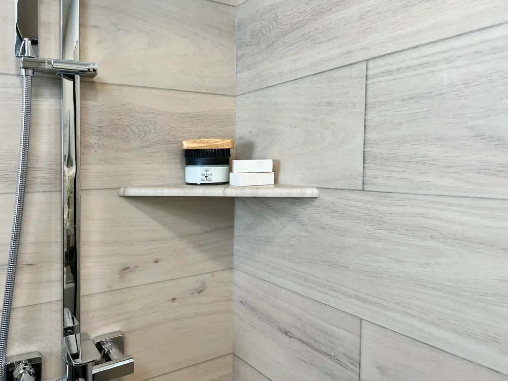 Light wood-grain tile shower niche with floating shelf and chrome fixtures