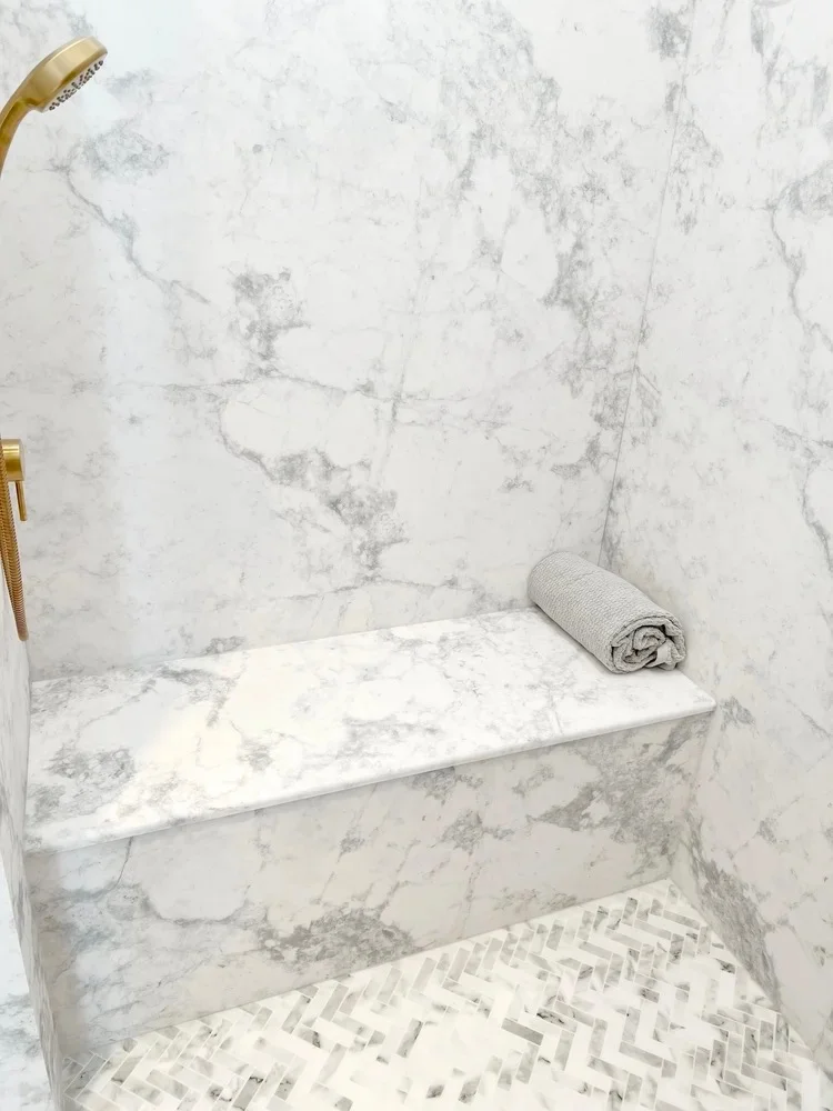 Marble shower with built-in bench, brass fixtures, and herringbone tile floor