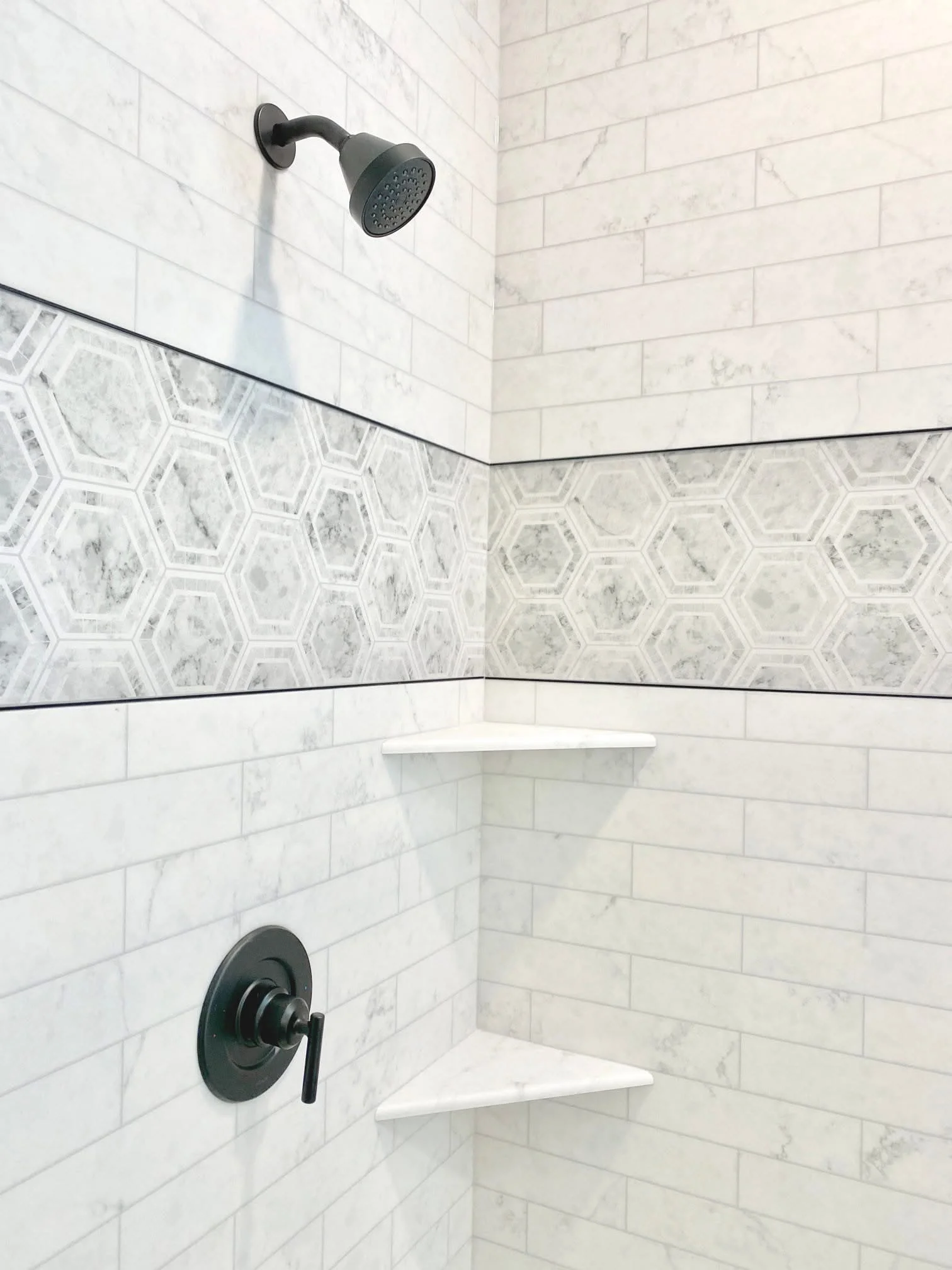 White marble subway tile shower with hexagon mosaic accent band and black matte fixtures