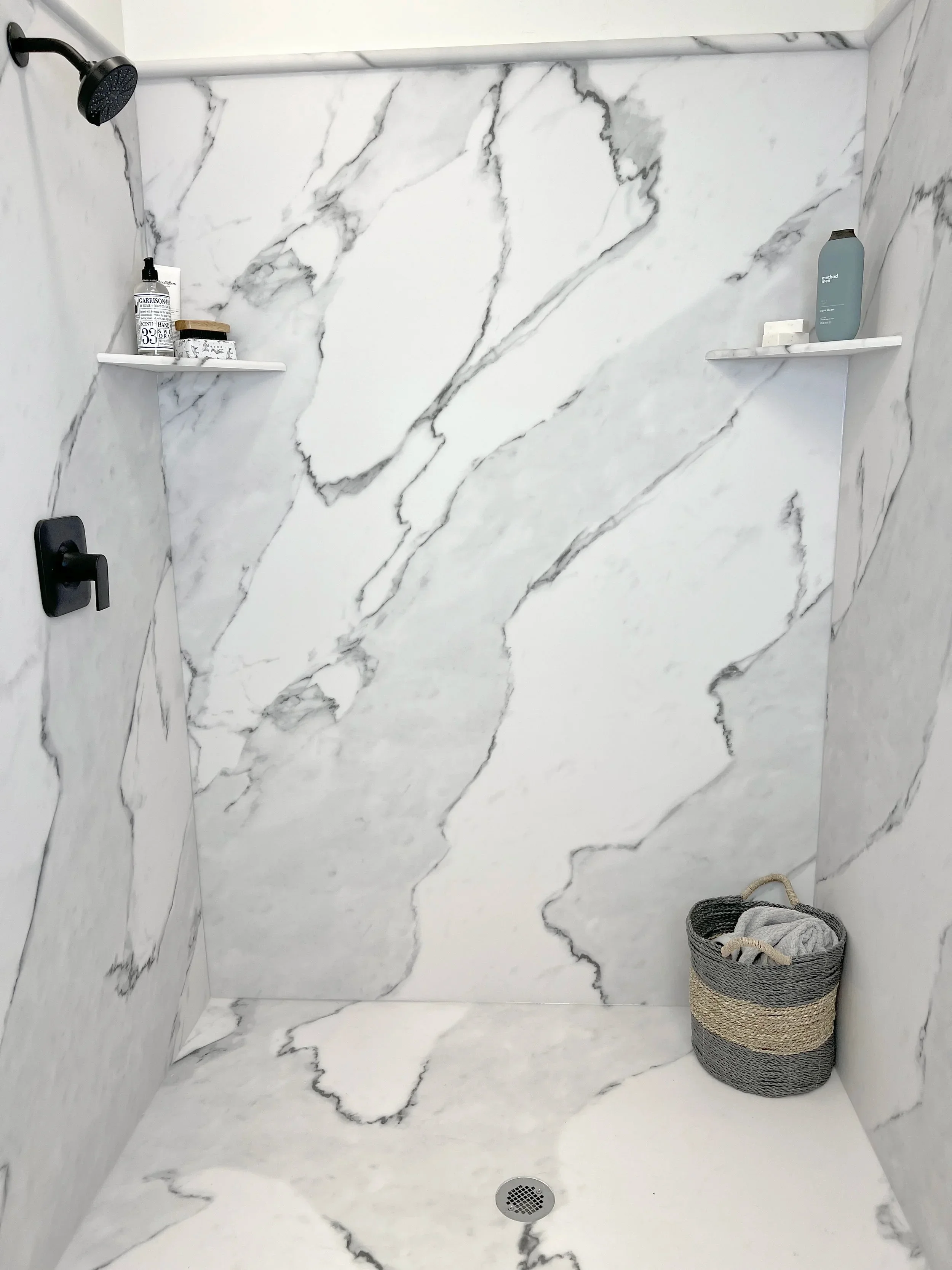 Marble tile shower with gray veining, floating shelves, and matte black fixtures