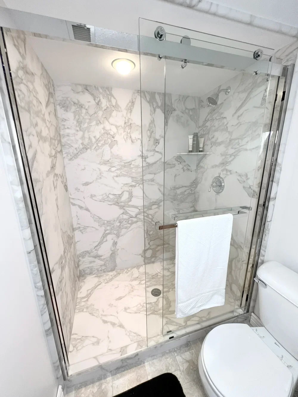 Frameless glass shower with Calcutta marble tile walls and floor, chrome fixtures