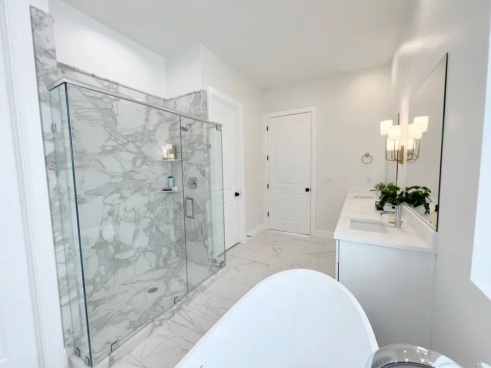 Bathroom with Calcutta marble tile, frameless glass shower enclosure, freestanding tub, and white vanity