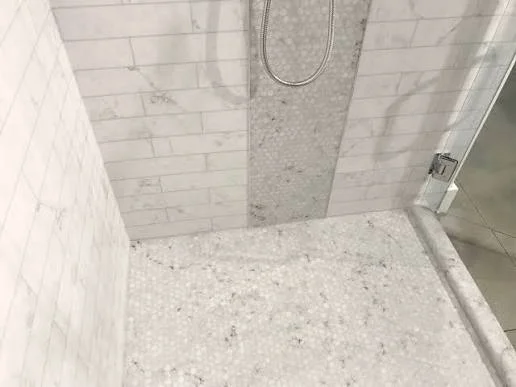 Walk-in shower with white subway tile walls and stone aggregate floor
