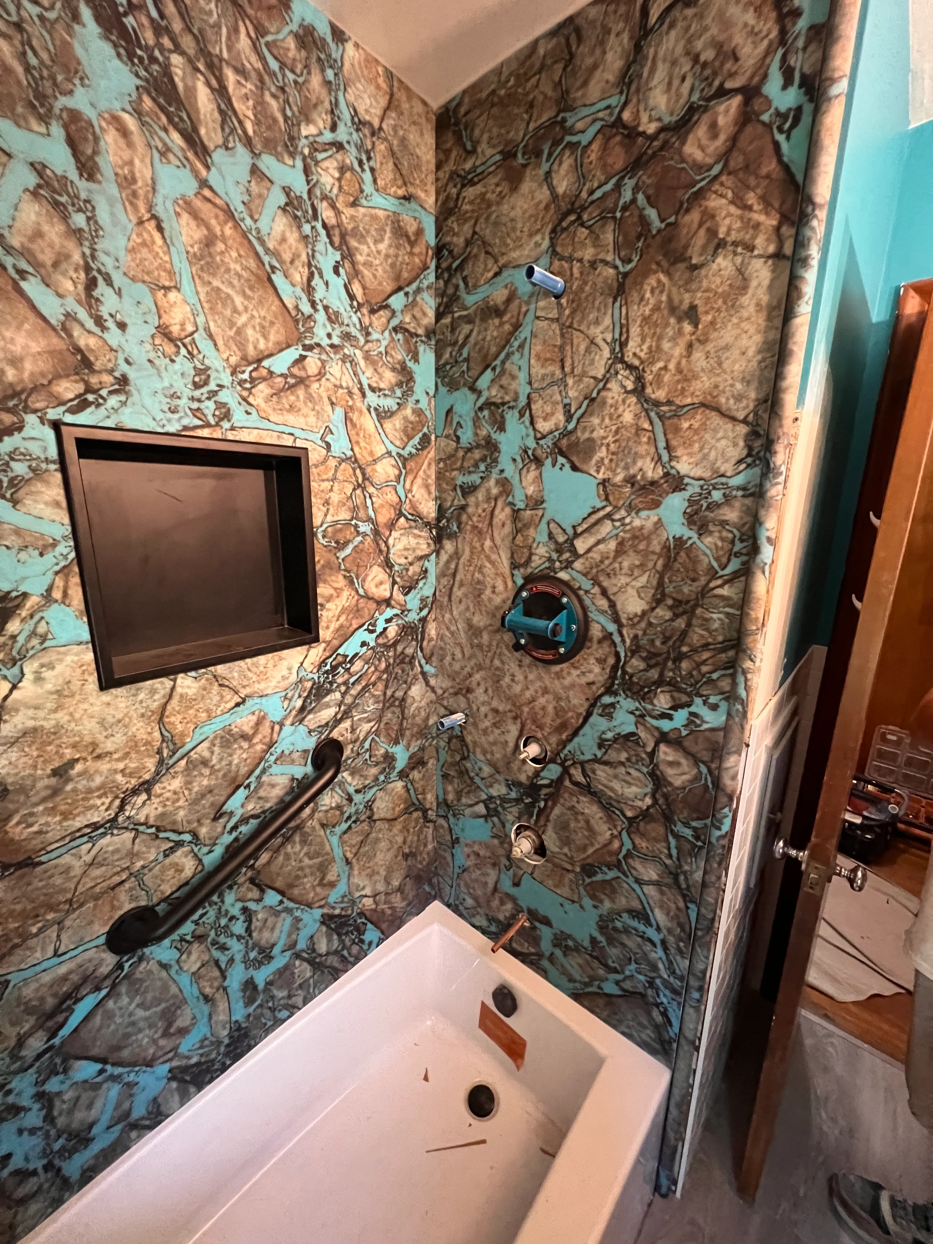 Shower enclosure with turquoise and brown patterned tile, recessed niche, and frameless glass door