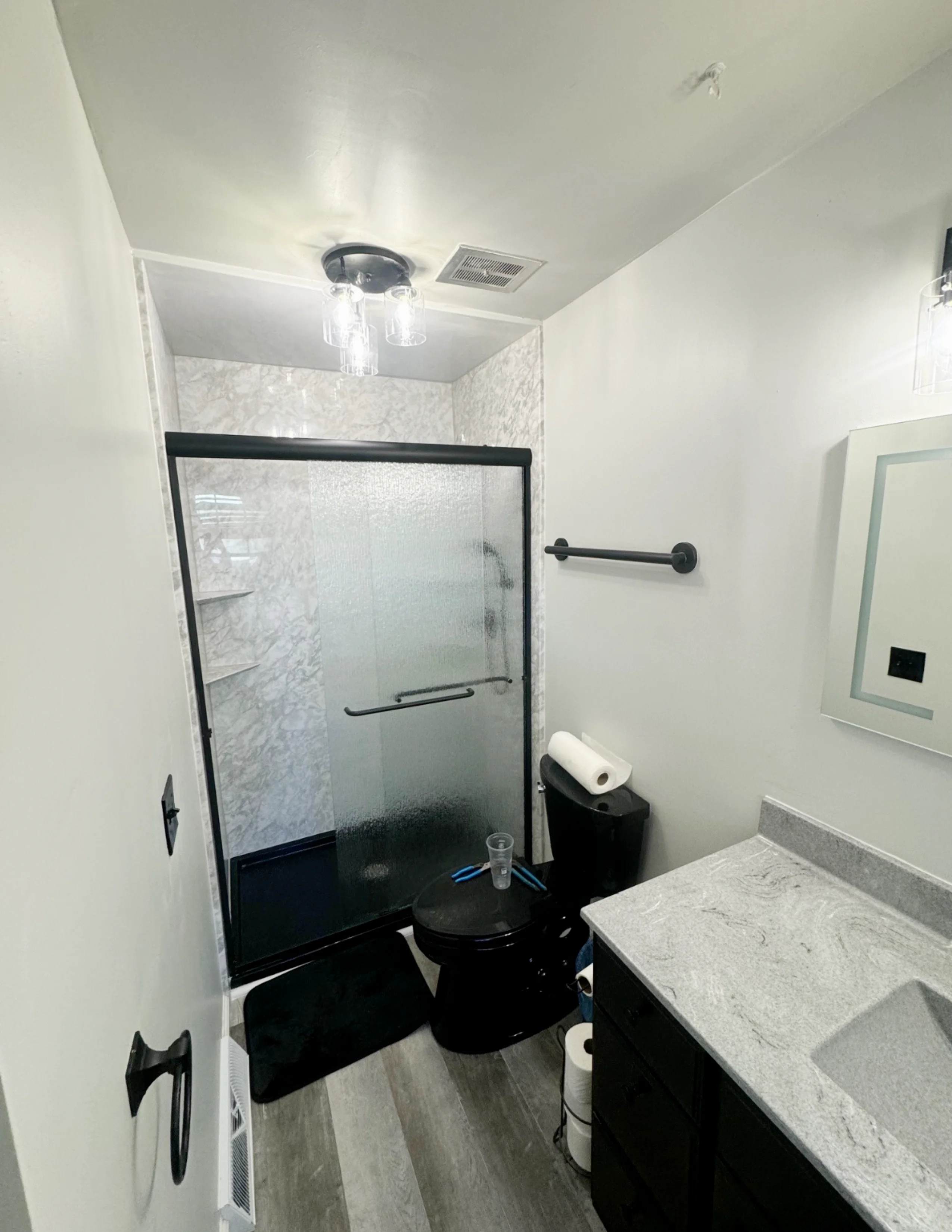 Black framed shower enclosure with marble tile, gray flooring, black vanity and fixtures