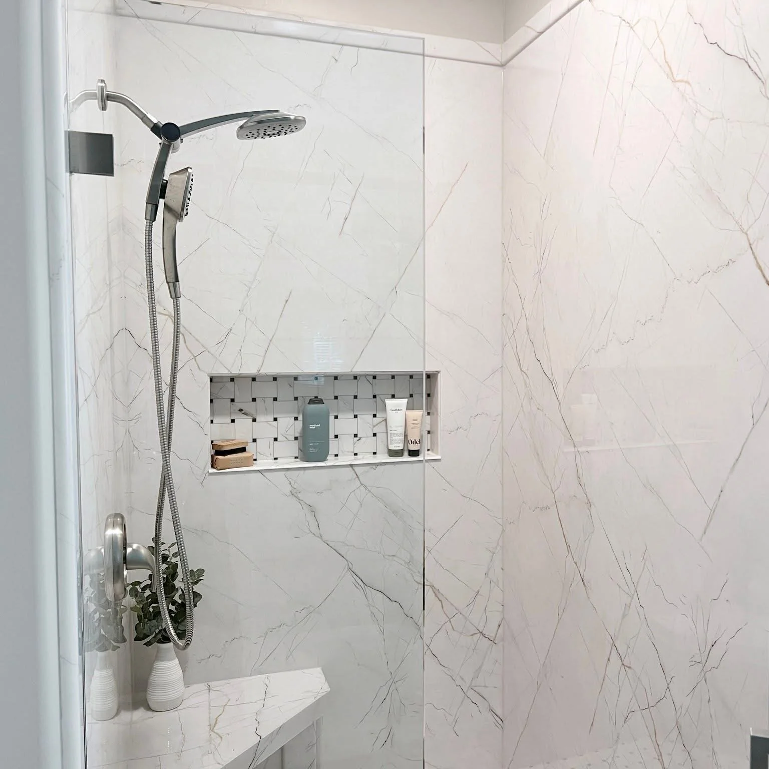 Marble tile shower with frameless glass door, dual showerheads, and built-in storage niche