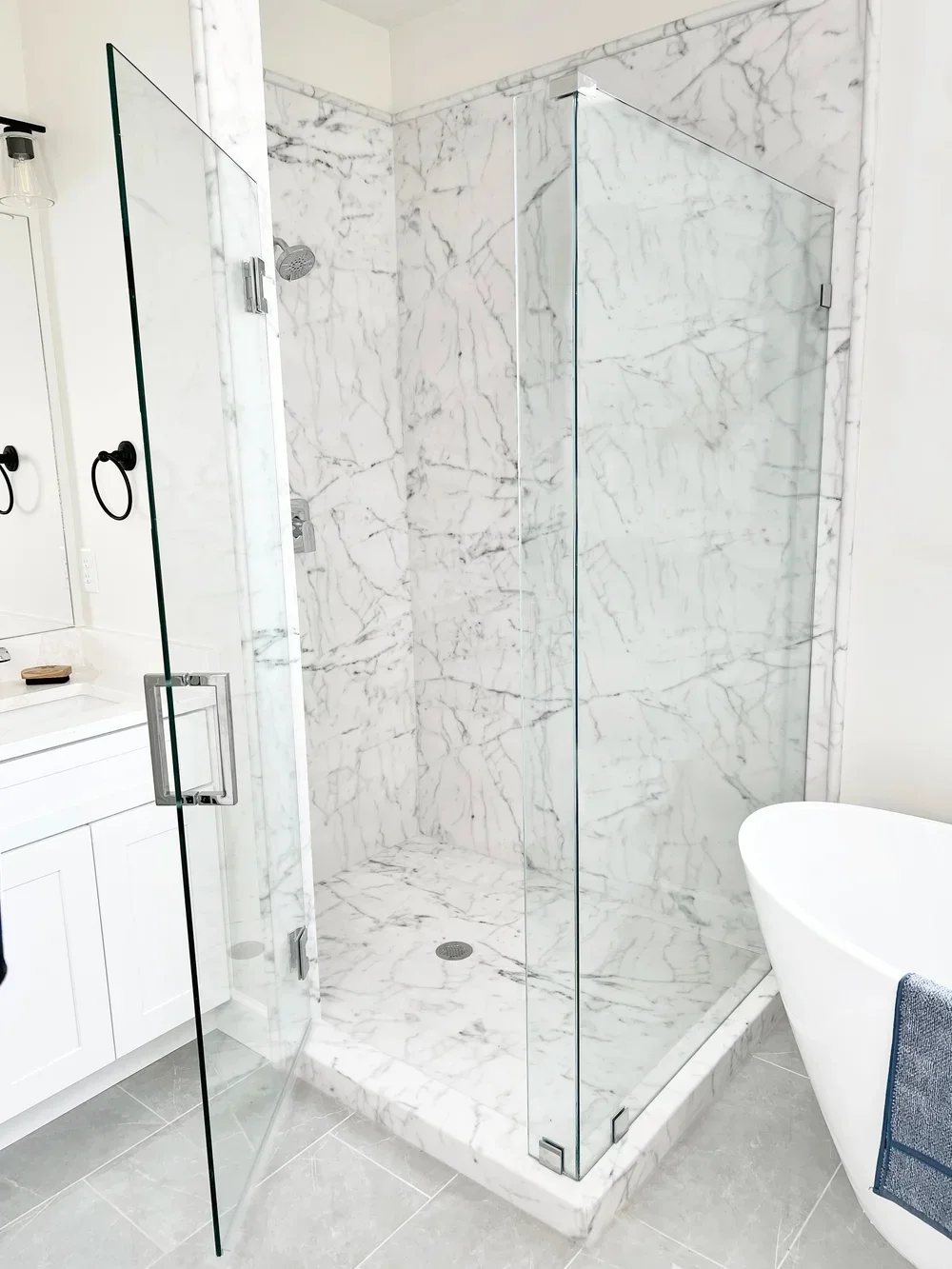 Frameless glass shower with Bianco Carrara marble tile walls and floor, chrome fixtures and rainfall showerhead
