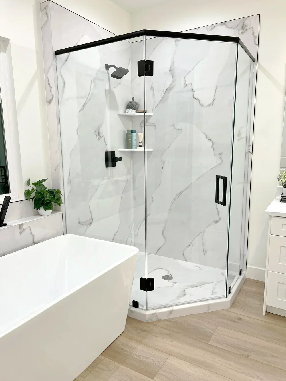 Frameless glass shower with marble tile walls, black hardware, and floating shelves