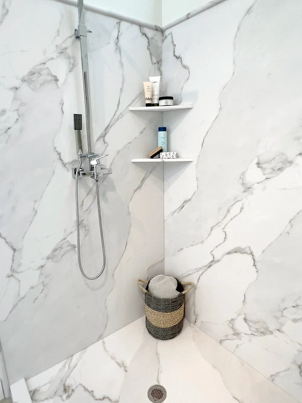Marble tile shower with chrome fixtures, floating shelves, and corner storage niche