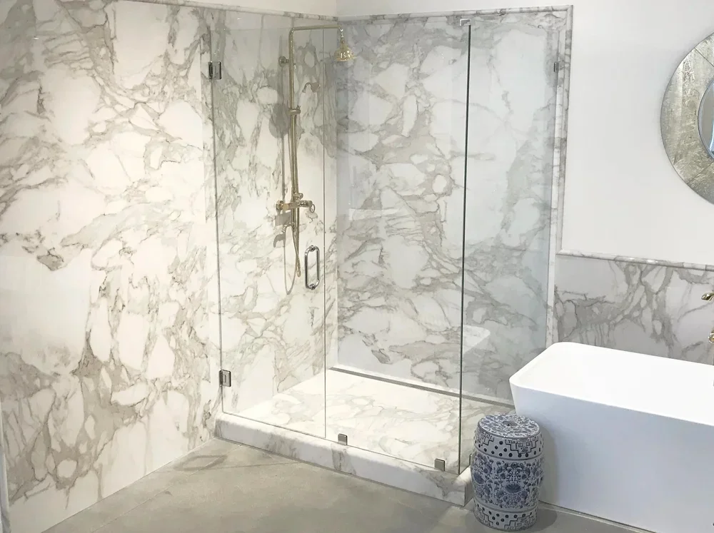Frameless glass shower with Calcutta marble walls and brushed nickel fixtures