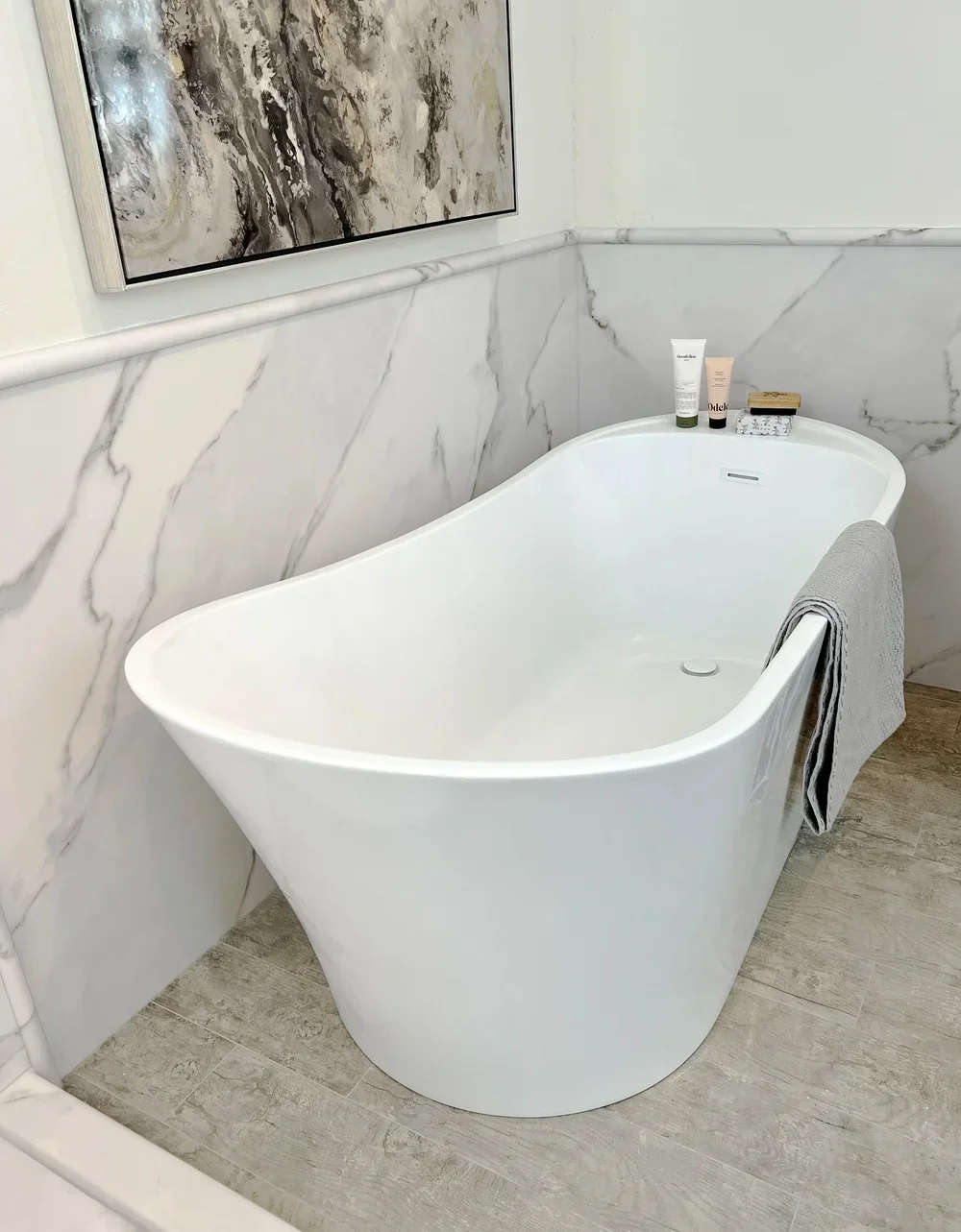 Freestanding white soaking tub with gray marble wainscoting surround and wood flooring