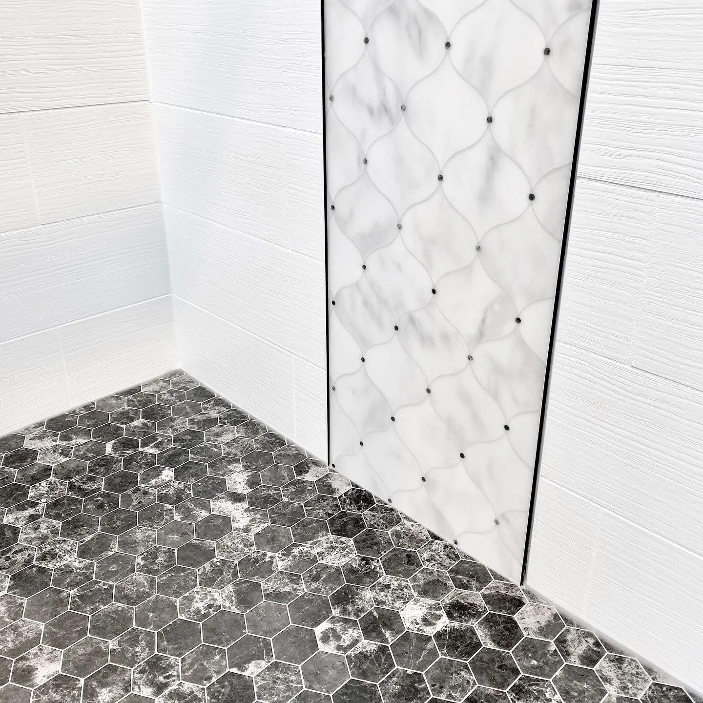 Shower corner with white subway tile walls, quilted marble glass panel, and dark hexagonal floor tile