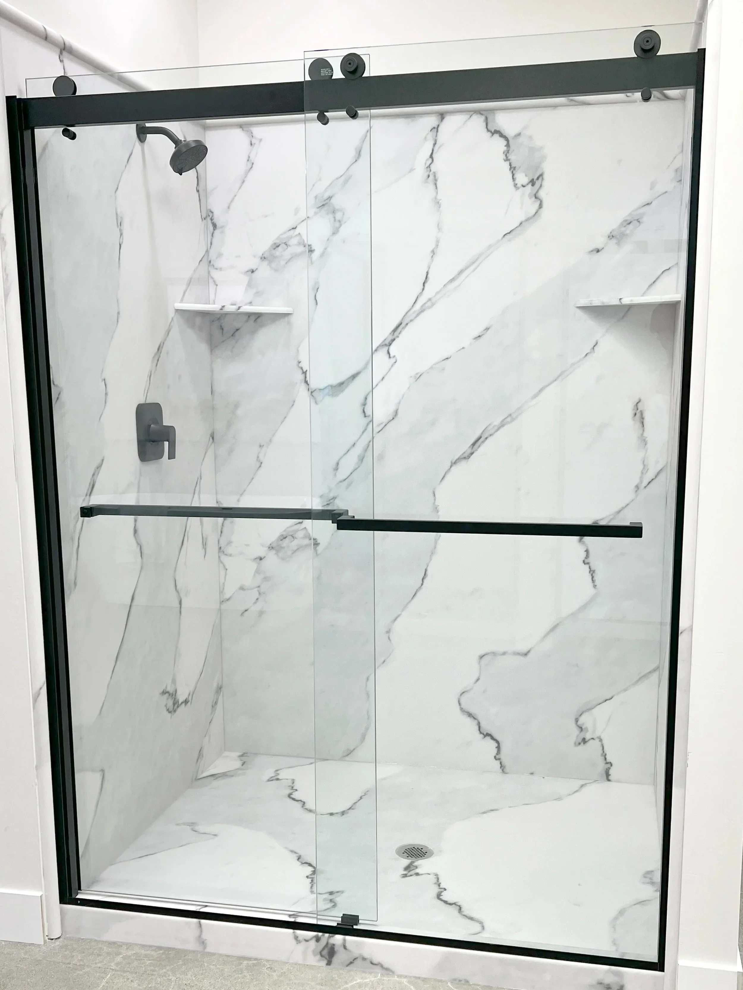 White marble tile shower with frameless sliding glass doors and matte black fixtures